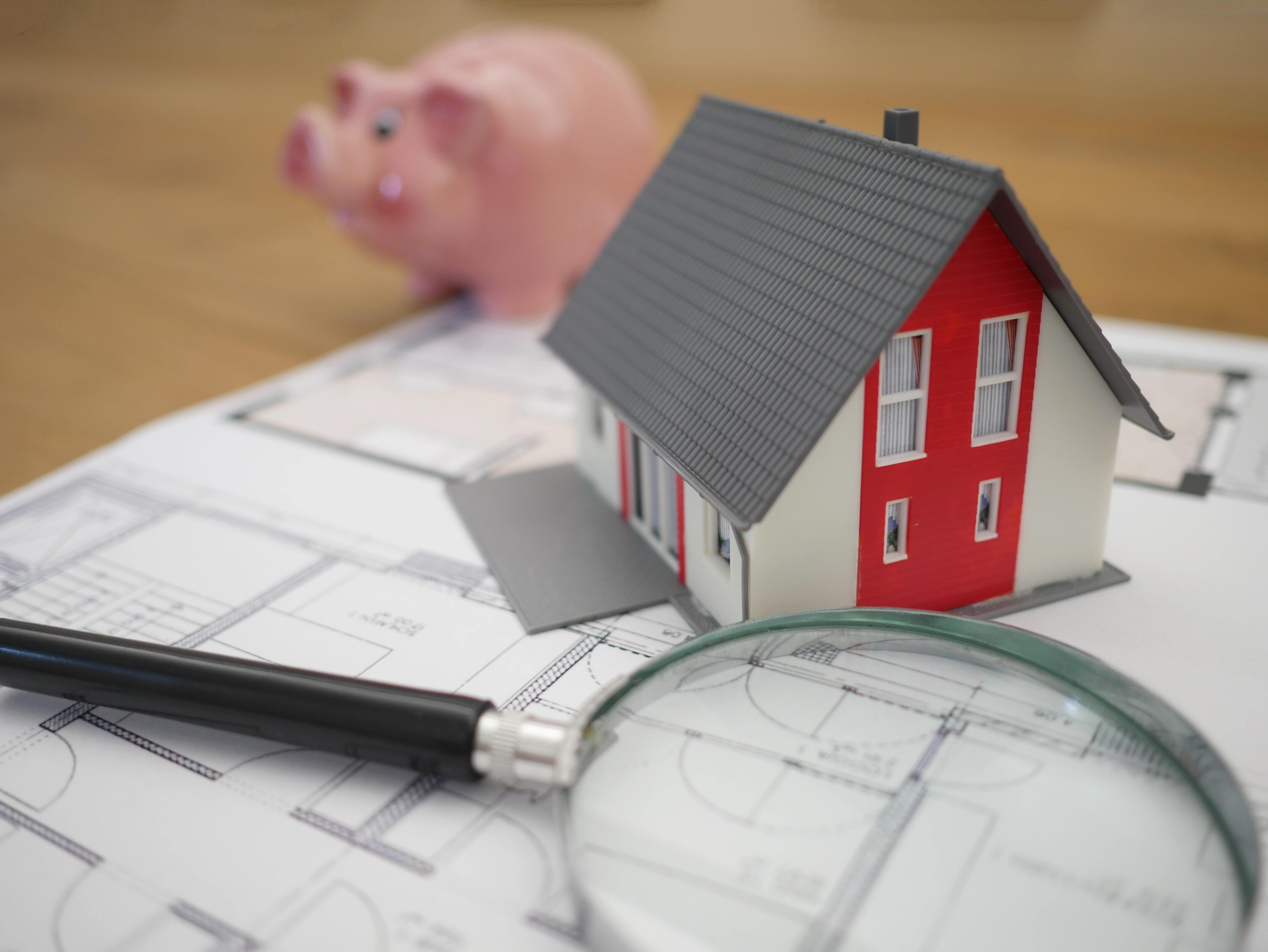 a toy house, magnifying glass and a piggy bank sit on a desk